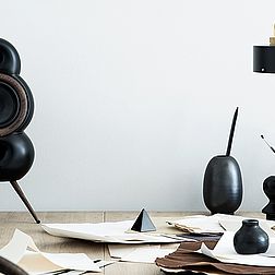 Ein Podspeaker Minipod in schwarz steht auf einem vollen Schreibtisch